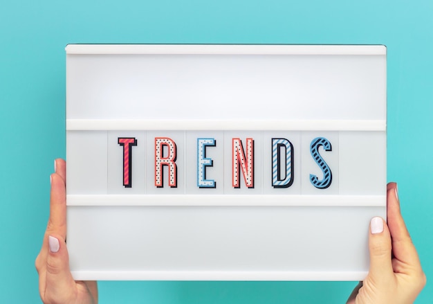 Female hands holds lightbox with the inscription trends on a blue background.