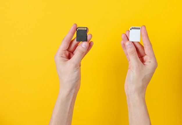 Female hands holds two SD memory cards on yellow. Minimalist Techno Concept.