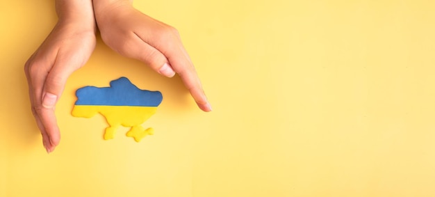 Female hands over a map of Ukraine in yellow and blue flag colors on a yellow background banner format Save Ukraine concept Copy space