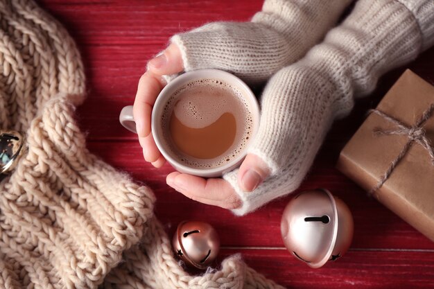 Female hands in mittens holding a cup of coffee on wooden background