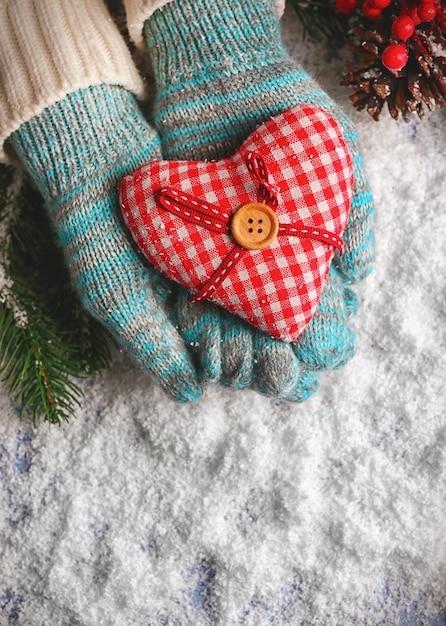 Female hands in mittens with decorative heart on snow background