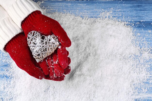 Female hands in mittens with decorative heart on snow background