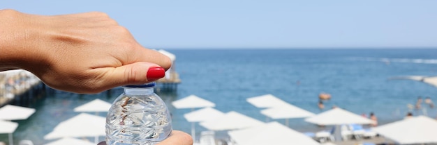 Female hands open a bottle of water on a hot beach blurry blue sky of the sea coast white