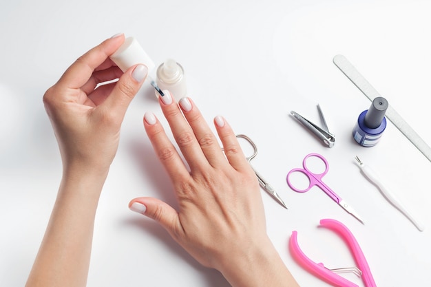 Female hands paint nails, next to lay down devices for nail care. girl does a manicure. on white background.