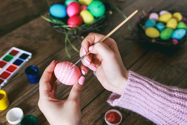 Female hands painting easter eggs on dark wooden table toned picture selective focus