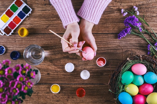 Female hands painting easter eggs on wooden table