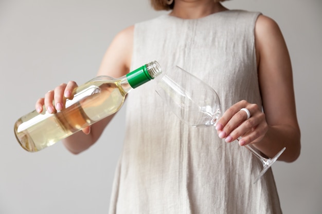 Female hands pour white wine from bottle to glass