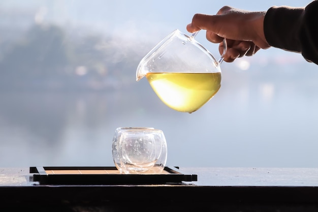 Female hands pouring hot tea with lake background at sunrise