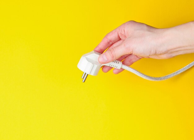 Female hands power plug on yellow background. Minimalism. Top view