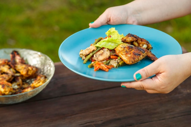 Female hands put a plate with chicken and vegetables on the table next to a dish with grilled chicken