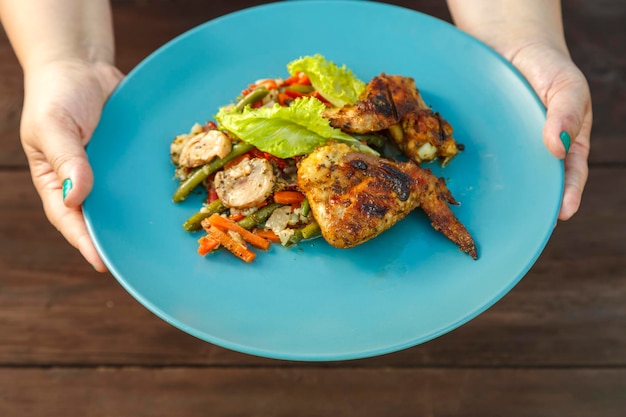 Female hands put a plate with grilled chicken and vegetables on the table on the street