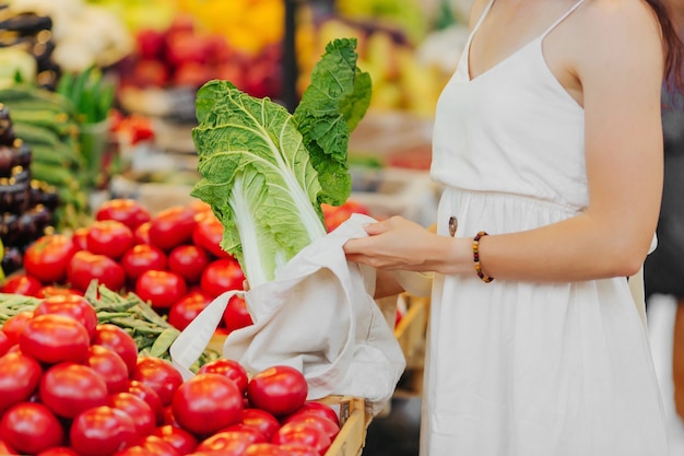 Female hands puts fruits and vegetables in cotton produce bag at food market. Reusable eco bag for shopping. Zero waste concept.