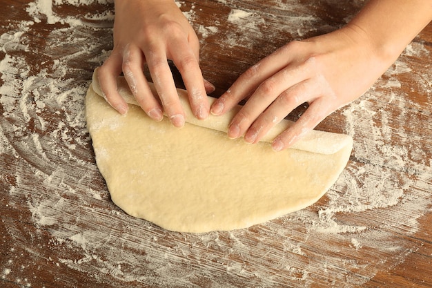 Female hands and rolled out dough on kitchen table close up