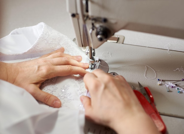 Female hands at sewing process and repairing white fabric on professional manufacturing machine Close up macro view