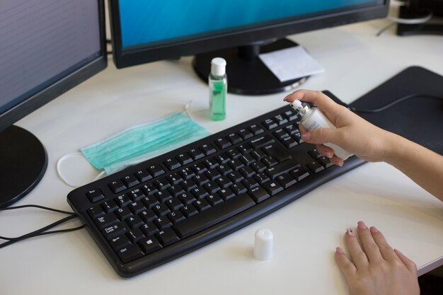 Female hands spray disinfectant spray on computer keyboard