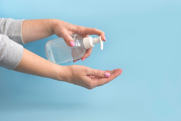 Female hands squeeze hand sanitizer gel from bottle on blue background. Hand disinfection and virus protection concept