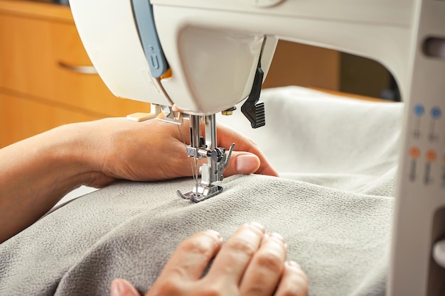 Female hands stitching gray fabric on modern sewing machine Close up view of sewing process