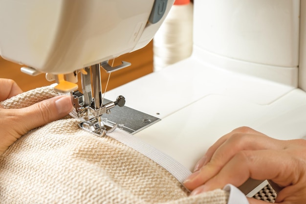 Female hands stitching white fabric on modern sewing machine Close up view of sewing process