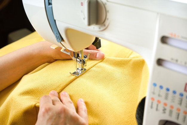 Female hands stitching yellow fabric on modern sewing machine Close up view of sewing process