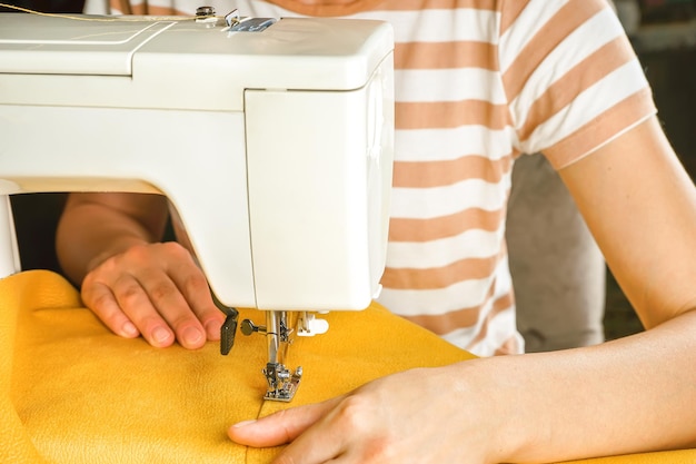 Female hands stitching yellow fabric on modern sewing machine Close up view of sewing process