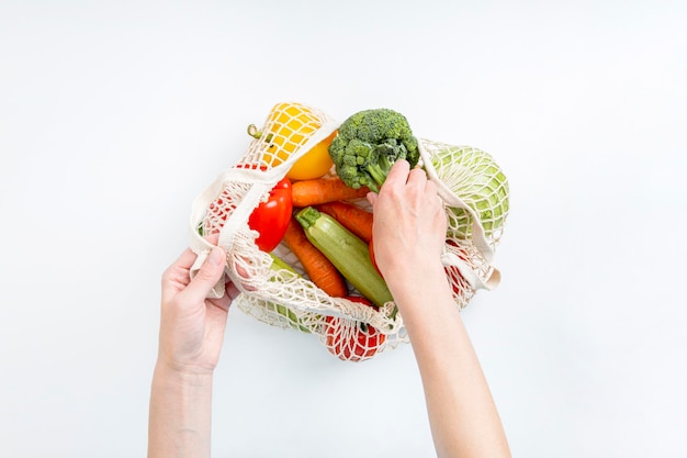 Female hands take out fresh vegetables from a bag on a white background Top view flat lay