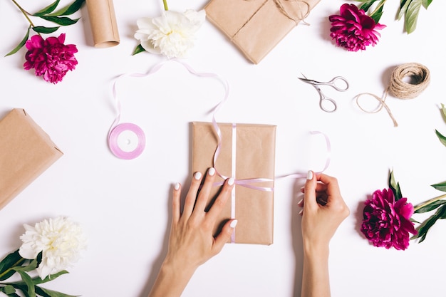 Female hands tie a ribbon on gift for a holiday on white table