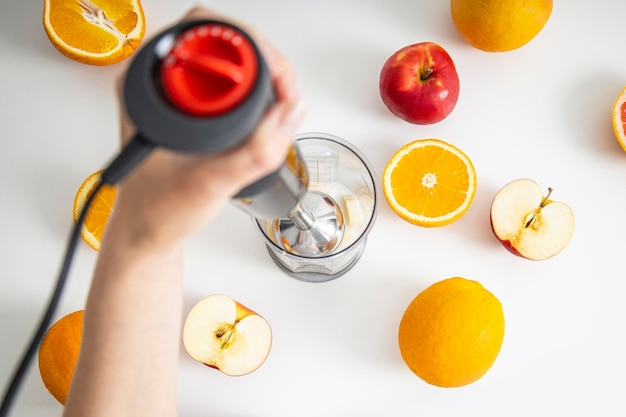 Female hands use a hand blender to mix fresh fruits to make a diet smoothie on a white background Top view flat lay