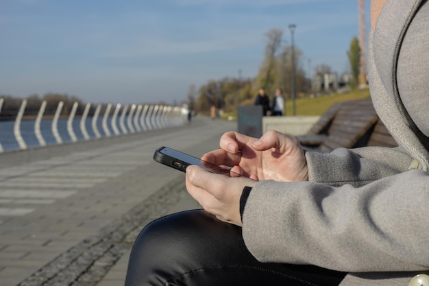 Female hands uses mobile phone sitting on bench Girl holds smartphone in hands outdoor