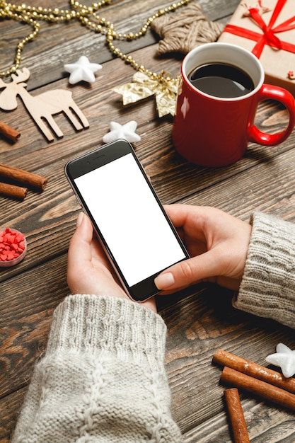 Female hands uses the phone sitting at a table with Christmas accessories