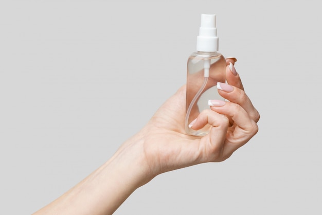 Female hands using hand sanitizer spray dispenser over light grey wall