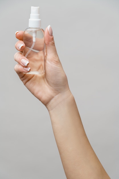 Female hands using hand sanitizer spray dispenser over light grey wall