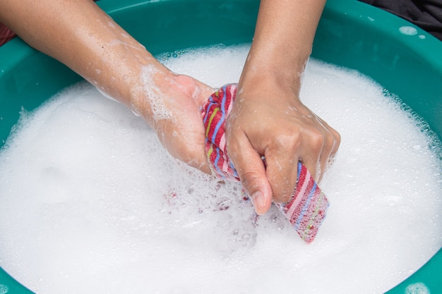 Female hands wash clothing by hand with detergent in basin.