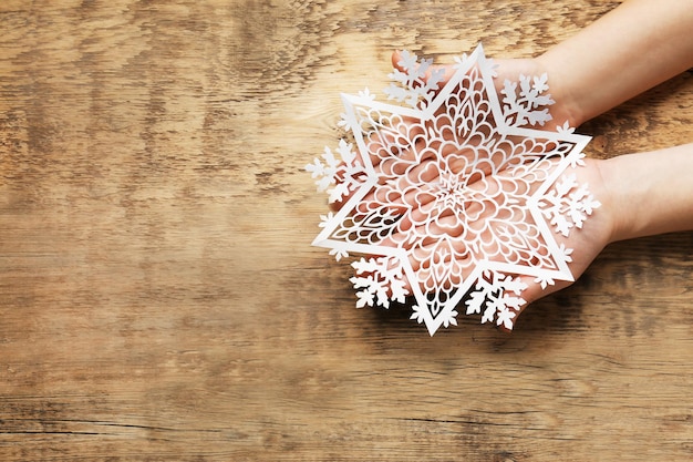 Female hands with beautiful paper snowflake on wooden background