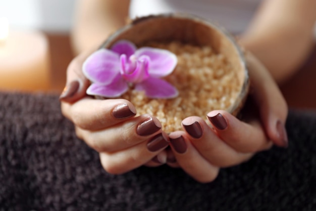 Female hands with brown manicure holding sea salt in bowl closeup