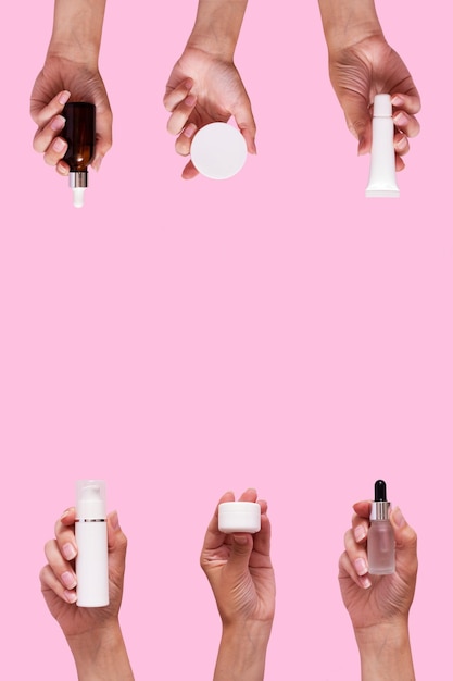 Female hands with cosmetic products in different containers and bottles mock up isolated on pink color background Vertical format