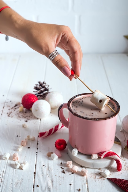 Female hands with Enamel cup of hot cocoa with mini marshmallows and candy canes 