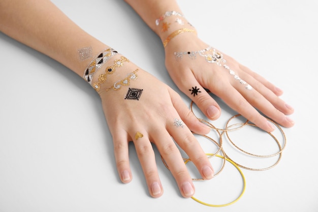 Female hands with flash tattoo holding bracelets on white background