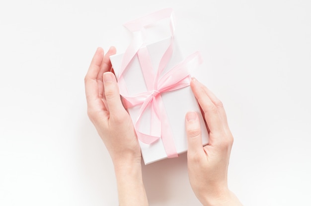 Female hands with a gift box with a pink ribbon.