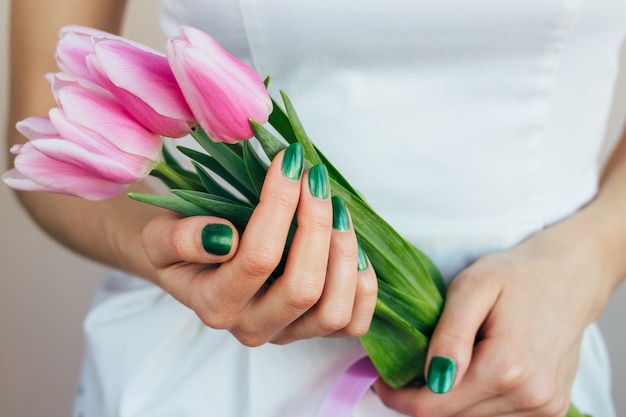 Female hands with green manicure holding pink tulips, close-up