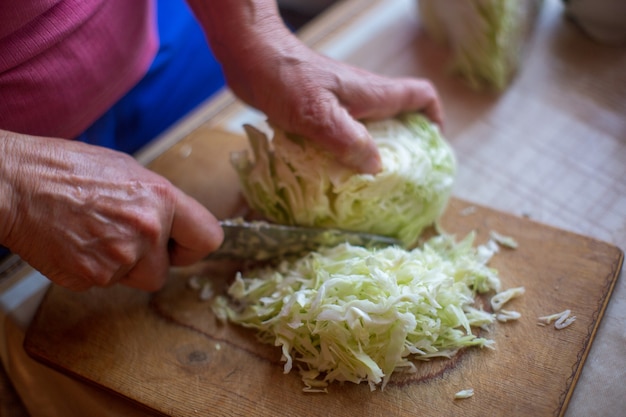 Female hands with a knife chop cabbage for cooking fresh salad