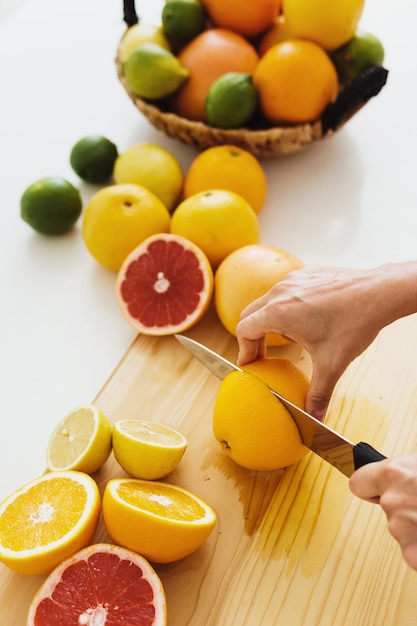 Female hands with knife slicing citrus fruits on cutting board for homemade fresh juice