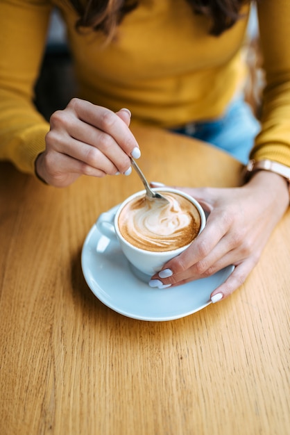 Female hands with latte on a wooden table.