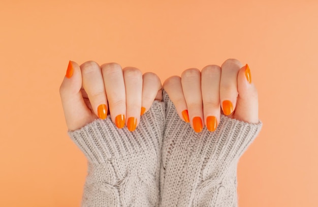 Female hands with orange manicure on orange background