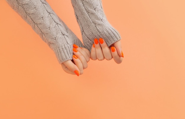 female hands with orange manicure on orange background