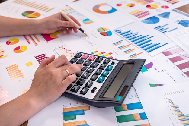 Female hands with pen and calculator on business graphs