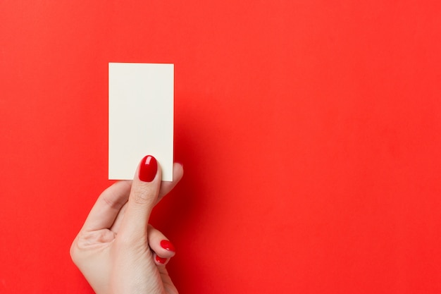 Female hands with red manicure holds a white blank business card