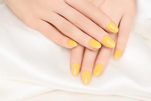 Female hands with yellow nail design on white fabric surface.