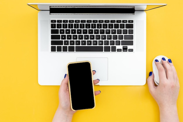 Female hands work behind a laptop on a yellow background top view