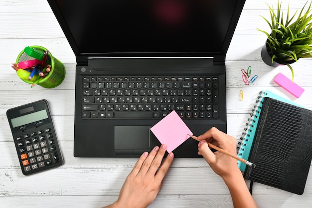 Female hands writing with a pencil on a pink sticky note