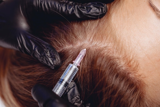 Female head closeup Women's hands in black gloves give injections to improve the structure of the hair